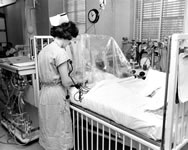 A nurse observes a patient under an oxygen tent.